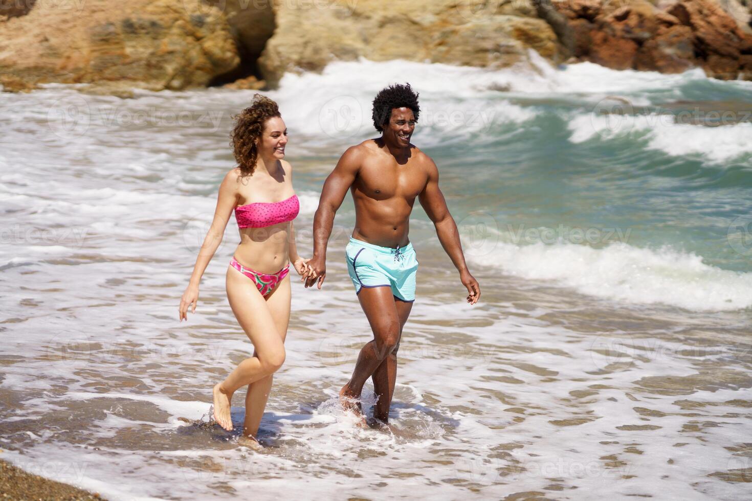 Happy diverse man and woman walking on wet coast photo