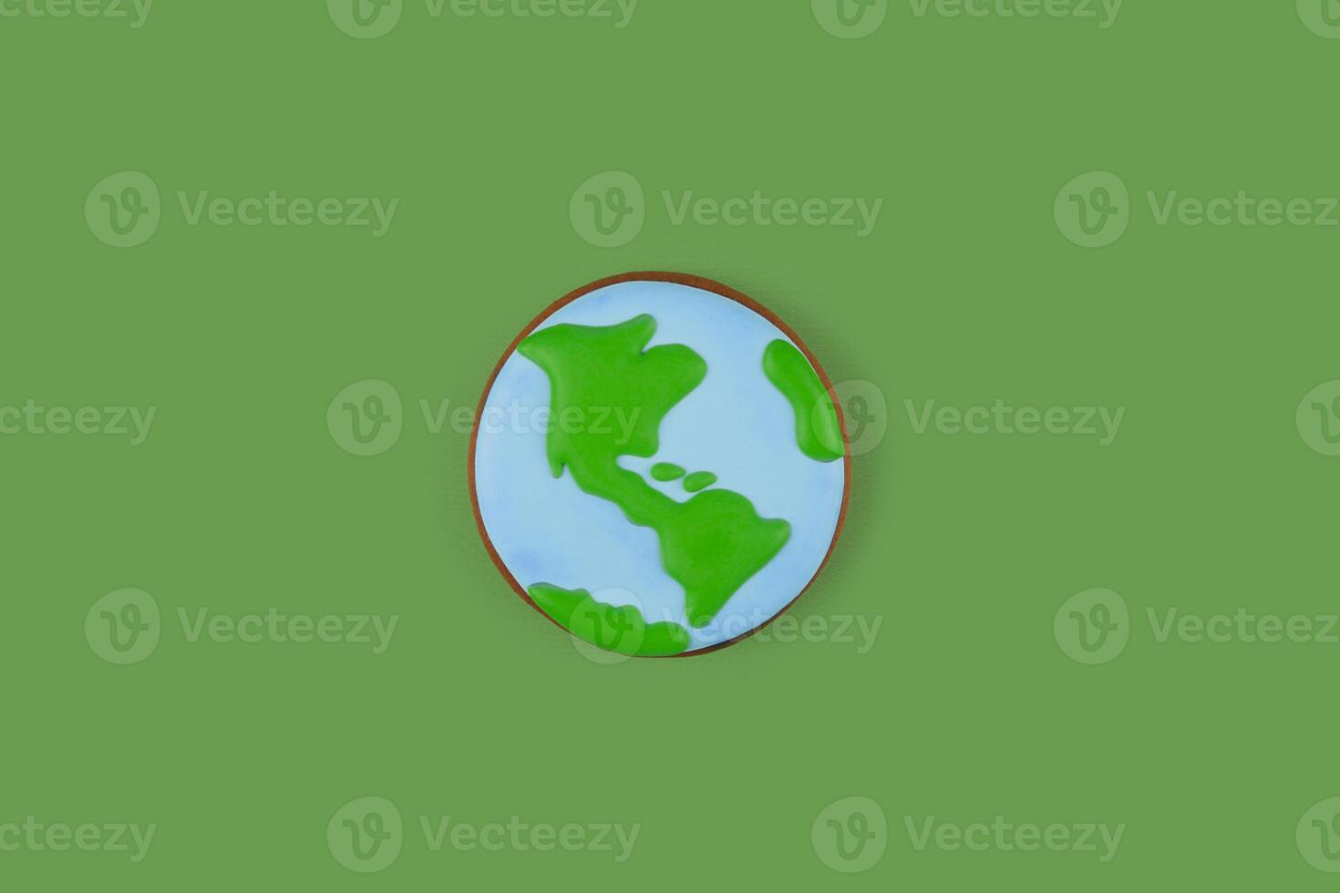 Earth Day concept. Single cookie in shape of Earth on green backdrop. photo