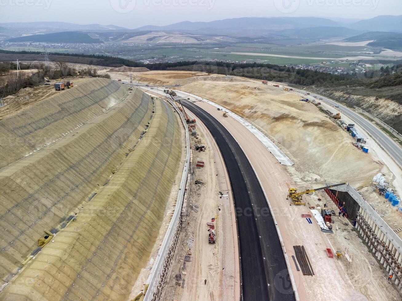 Mountain road constraction. Workers reinforce the slope over the new road. Road construction in progress on slope nature canyon. Infrastructure development and logistics. Aerial drone shot photo