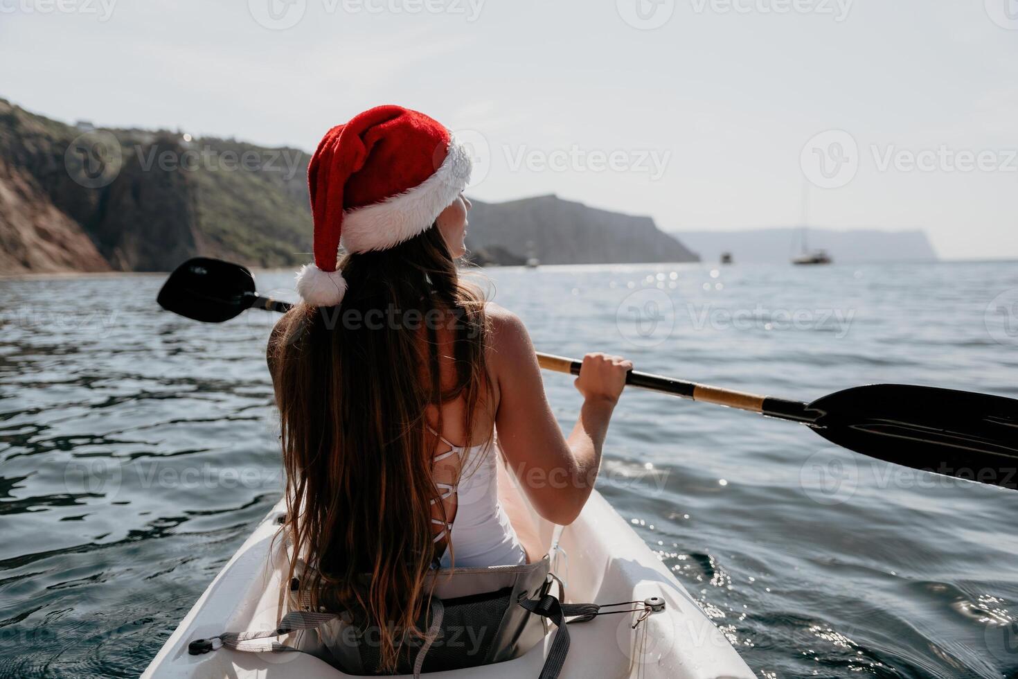 Woman in kayak back view. Happy young woman in Santa hat floating in kayak on calm sea. Summer holiday vacation and cheerful female people relaxing having fun on the boat. photo