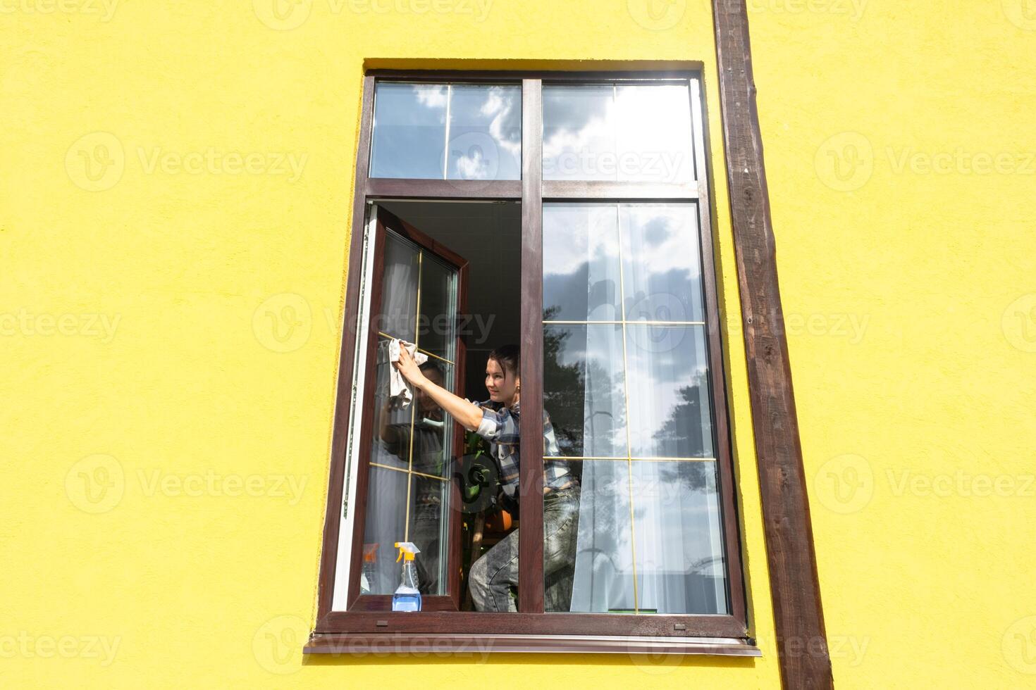 un mujer a mano lavados el ventana de el casa con un trapo con un rociar limpiador y un fregona afuera. la seguridad a altura, restaurar orden y limpieza en el primavera, limpieza Servicio foto