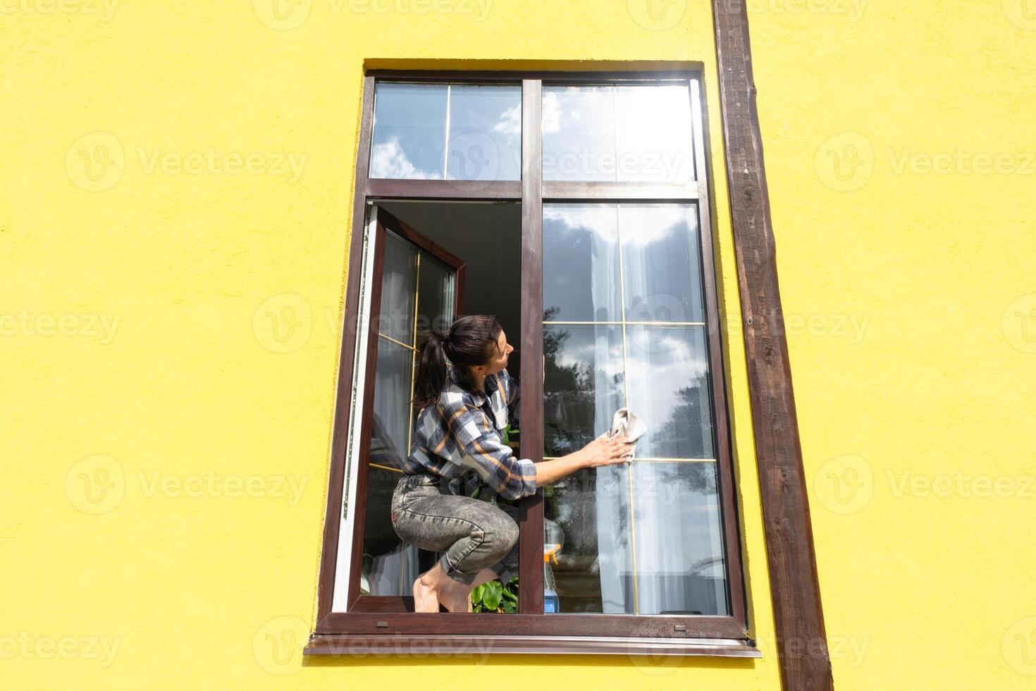 un mujer a mano lavados el ventana de el casa con un trapo con un rociar limpiador y un fregona afuera. la seguridad a altura, restaurar orden y limpieza en el primavera, limpieza Servicio foto