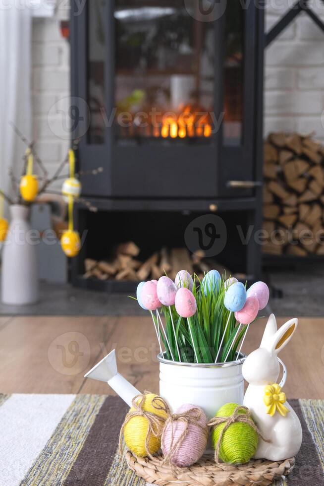 Easter decor near fireplace stove with fire and firewood. Cozy home hearth in interior with potted plans, colorful easter eggs, easter bunny and bouquet. Spring in a country house photo