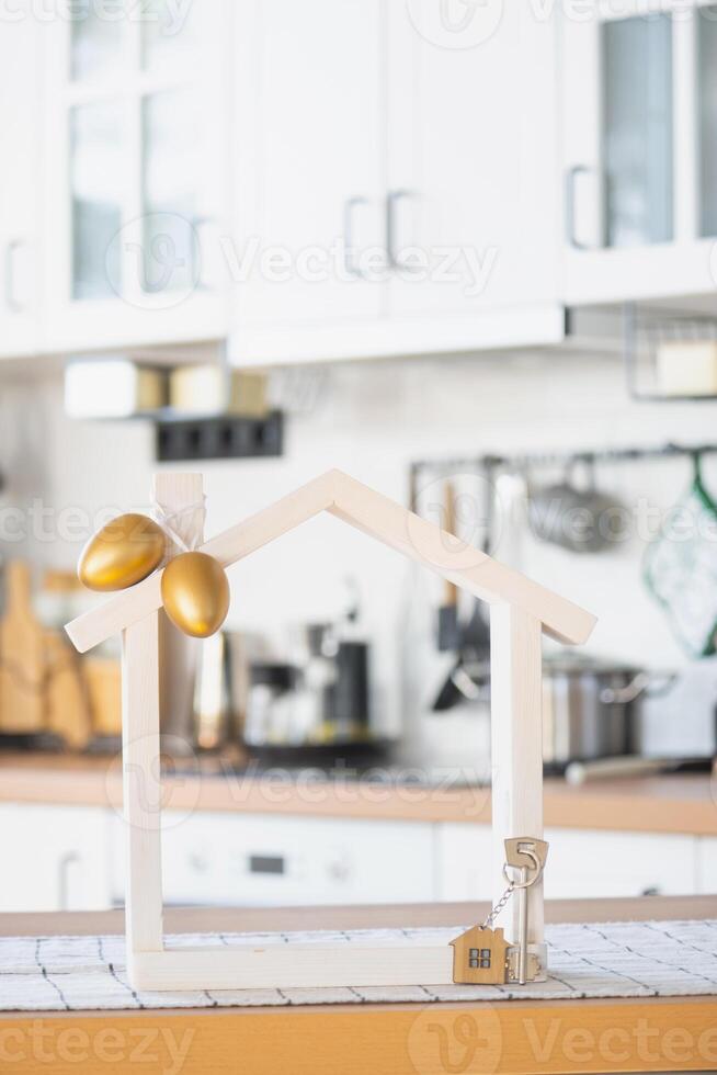 Key and tiny house of cozy home with Easter decor with color eggs on table of kitchen. Building, design, project, moving to new house, mortgage, insurance, rent and purchase real estate photo