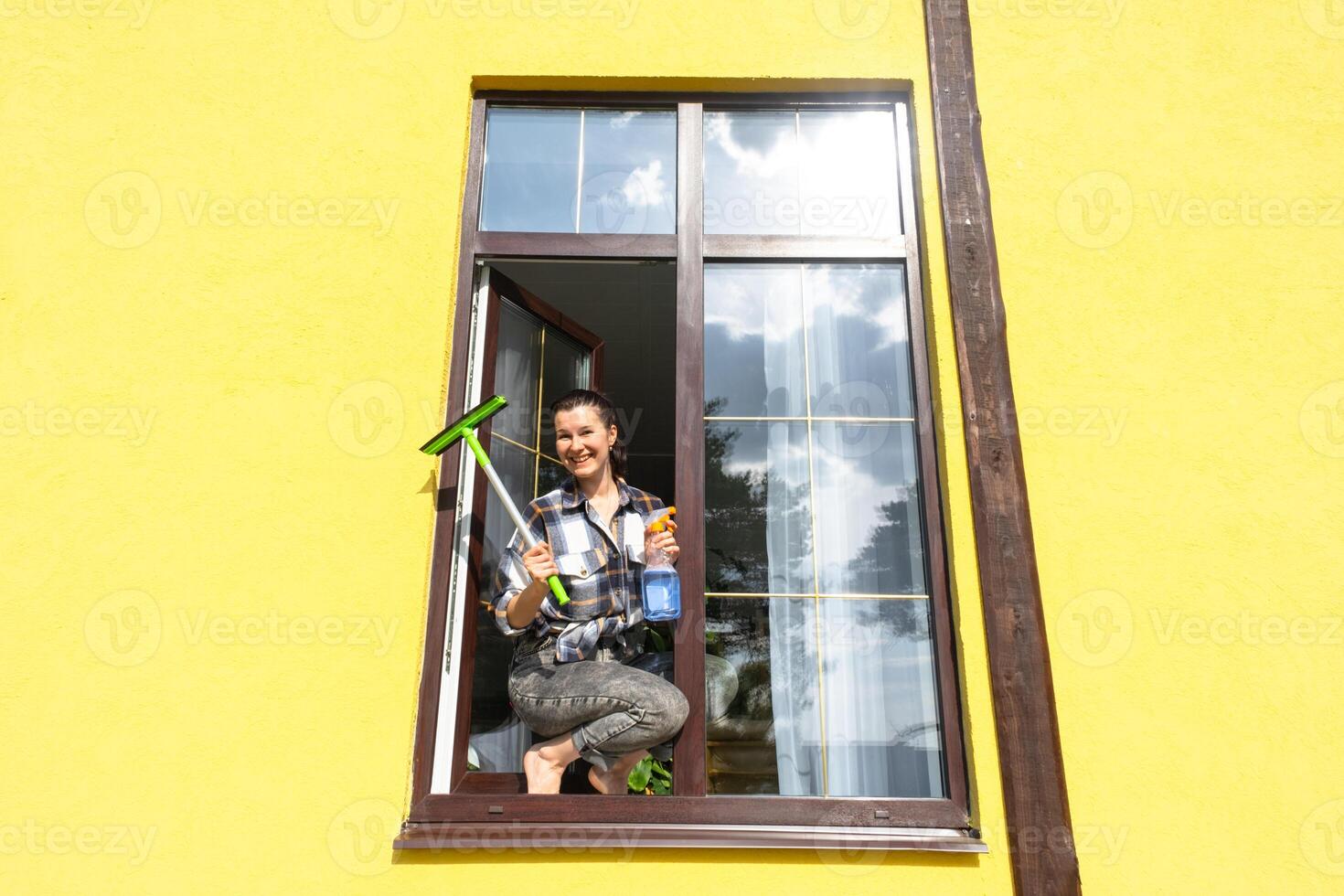 A woman manually washes the window of the house with a rag with a spray cleaner and a mop outside. Safety at height, restoring order and cleanliness in the spring, cleaning service photo