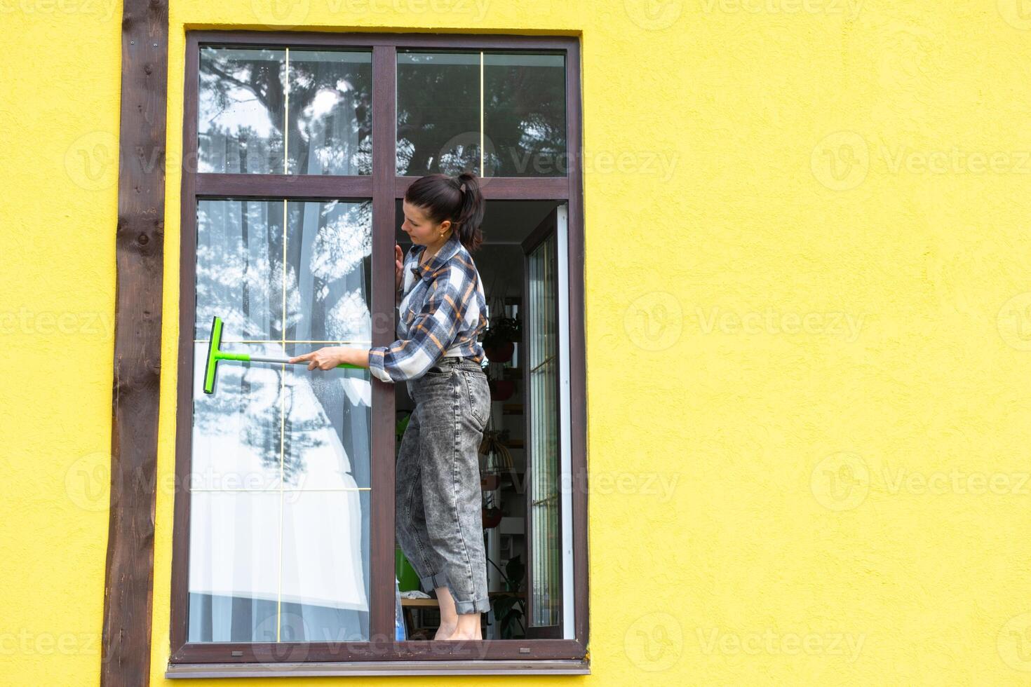 un mujer a mano lavados el ventana de el casa con un trapo con un rociar limpiador y un fregona afuera. la seguridad a altura, restaurar orden y limpieza en el primavera, limpieza Servicio foto