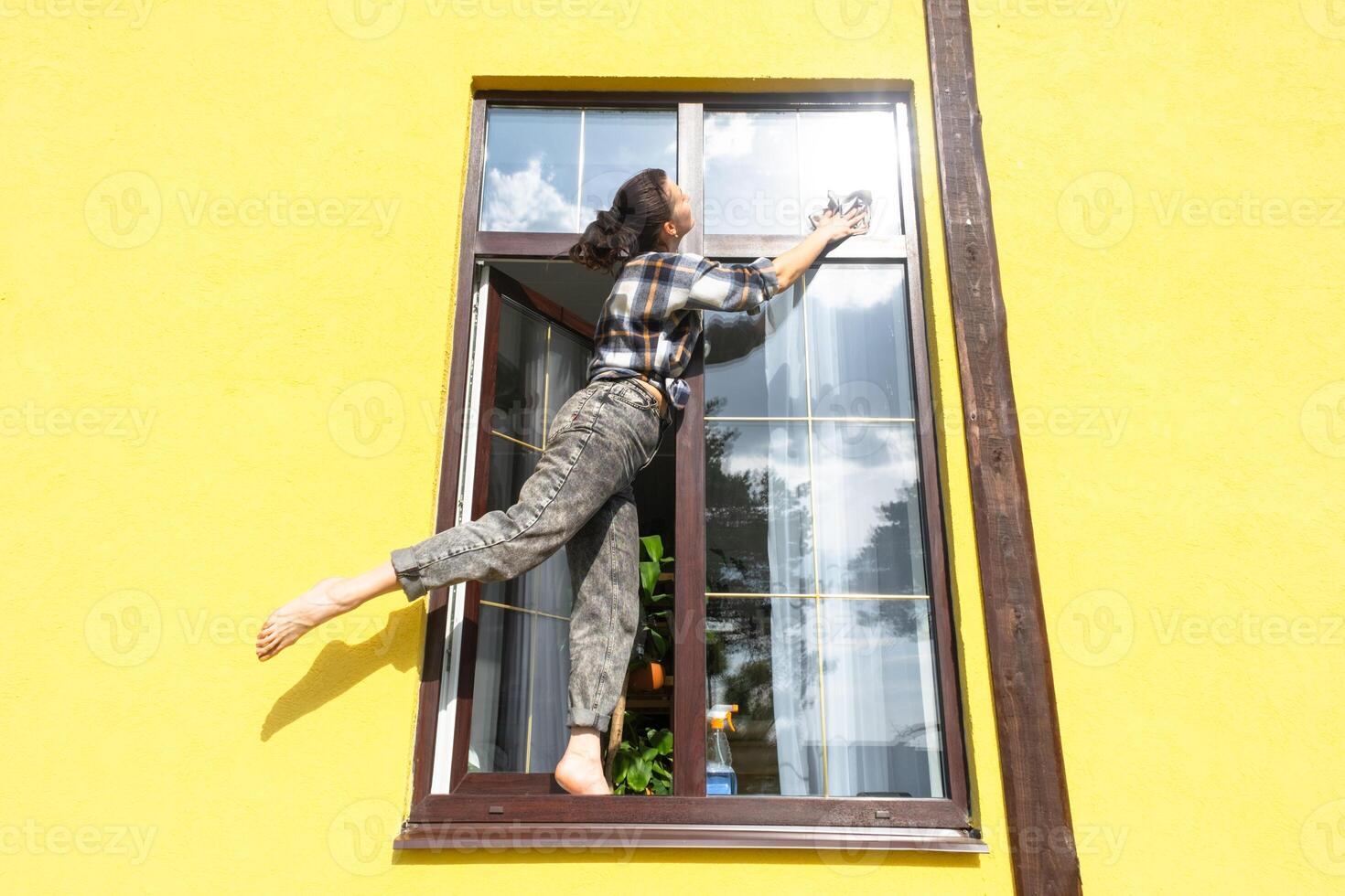 un mujer a mano lavados el ventana de el casa con un trapo con un rociar limpiador y un fregona afuera. la seguridad a altura, restaurar orden y limpieza en el primavera, limpieza Servicio foto