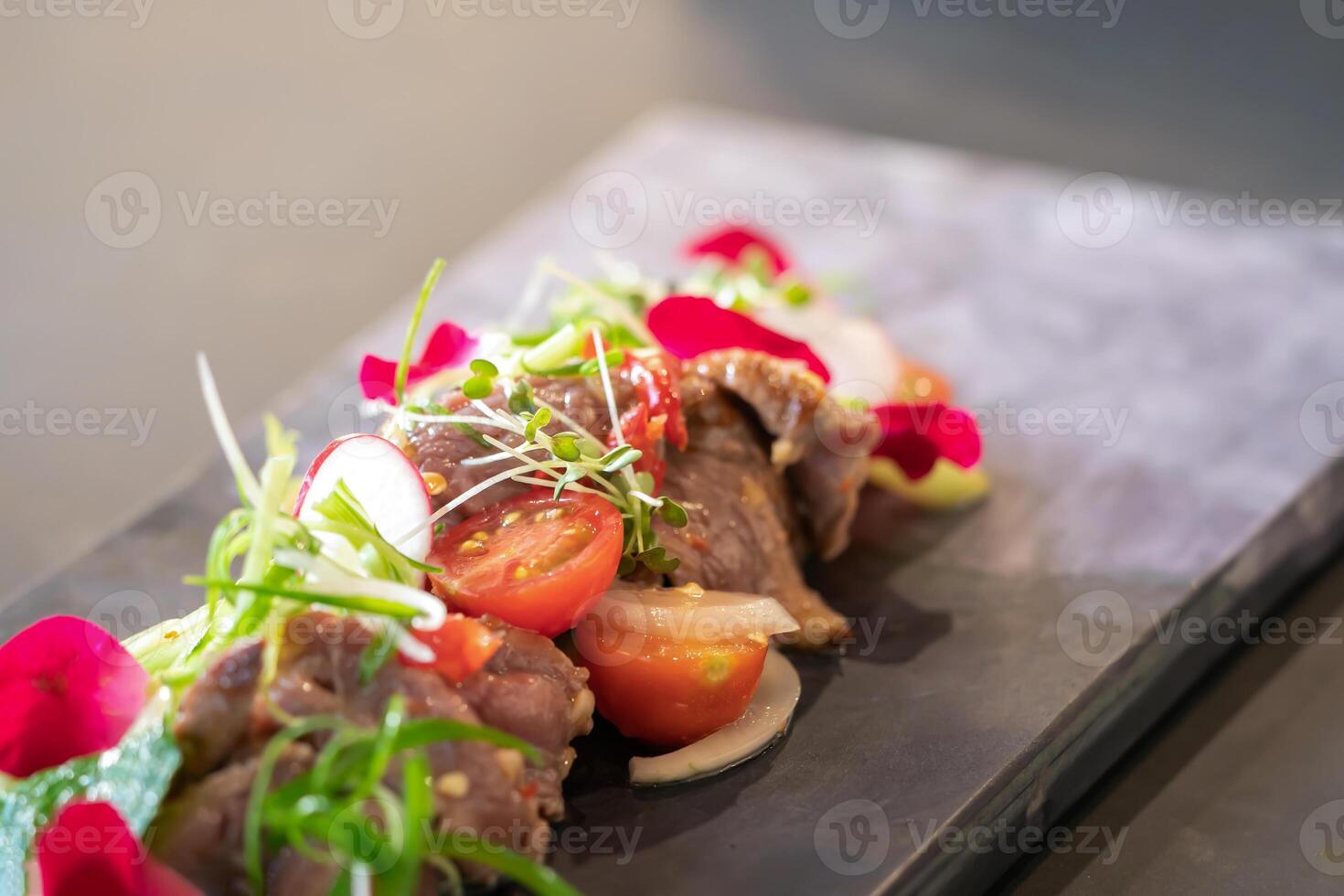 cerca arriba a picante tailandés carne de vaca ensalada adornado en parte superior con berro y micro hierba estaba poner en un rectangular Roca lámina. foto