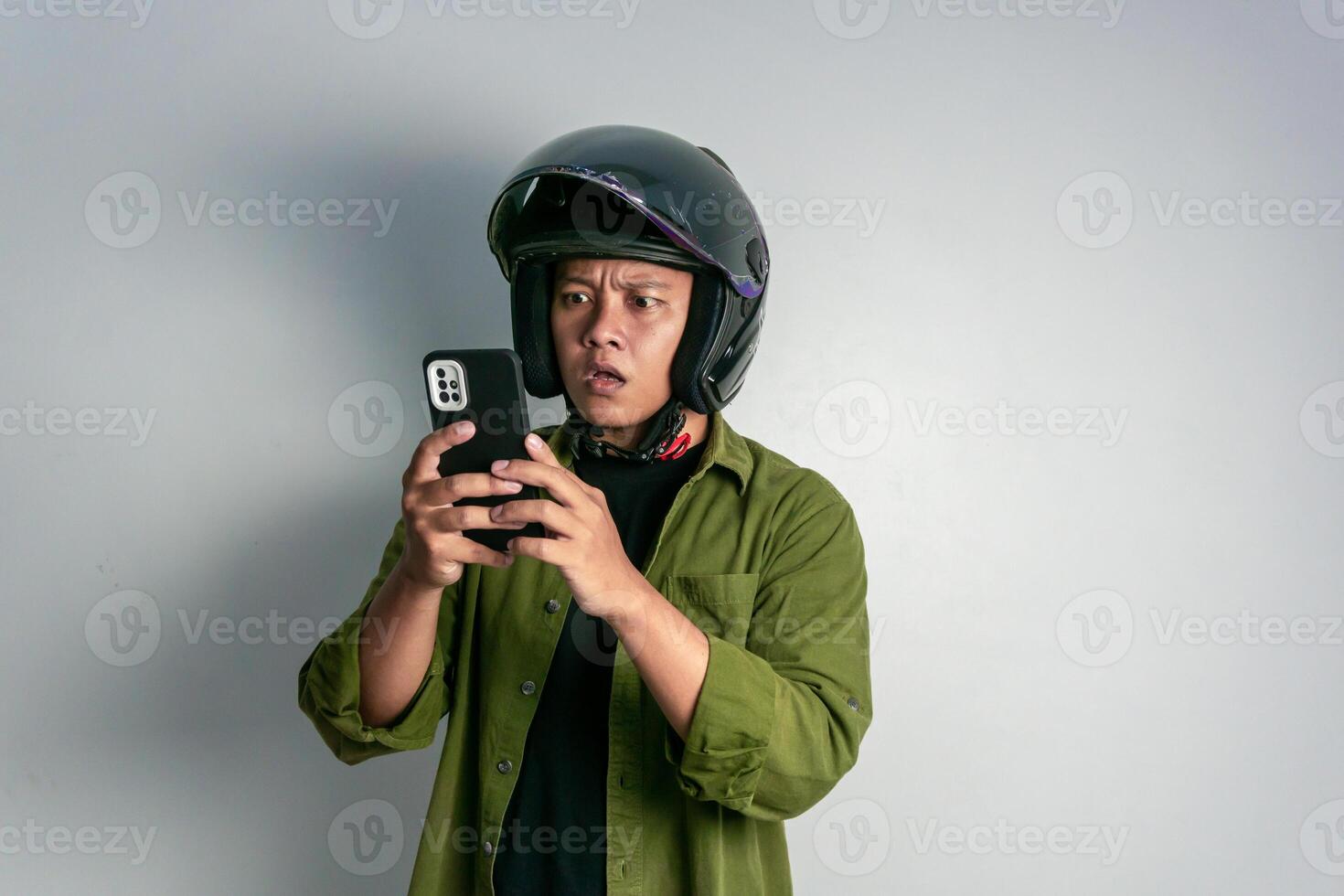 adulto asiático hombre confuso cuando mirando a su teléfono de mano mientras vistiendo motocicleta casco. hombre mirando a su teléfono con conmocionado expresión foto