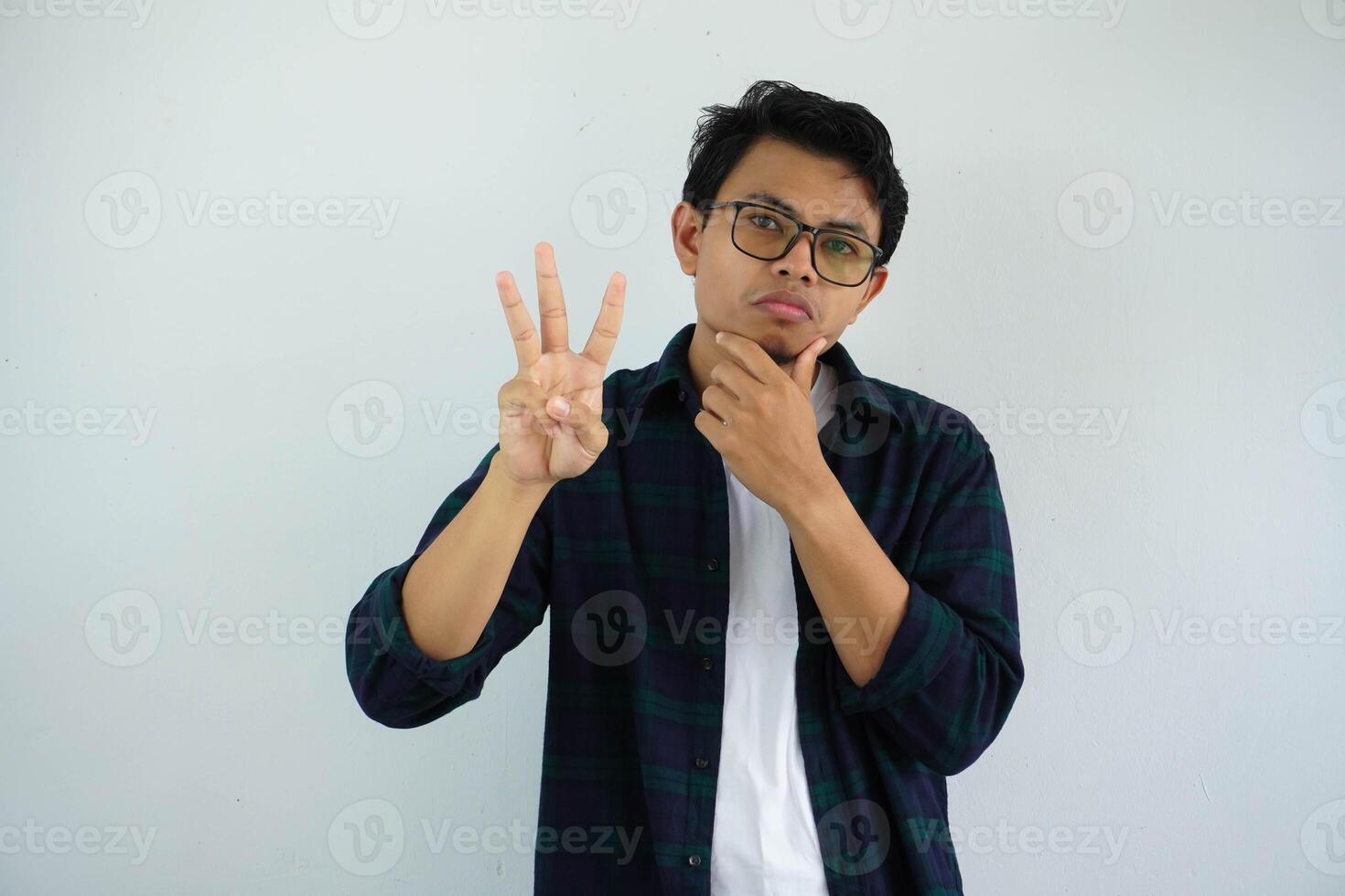 young asian man showing curious face expression while giving three fingers sign isolated on white background photo