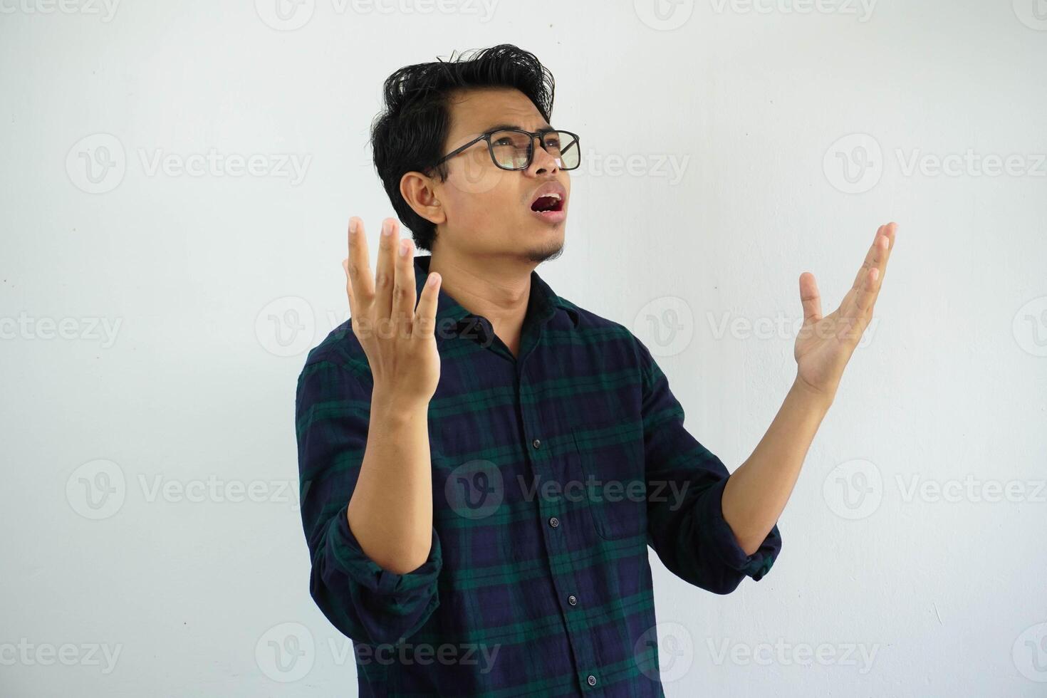 young Asian man looks up showing a regretful expression with his arms open isolated on white background photo