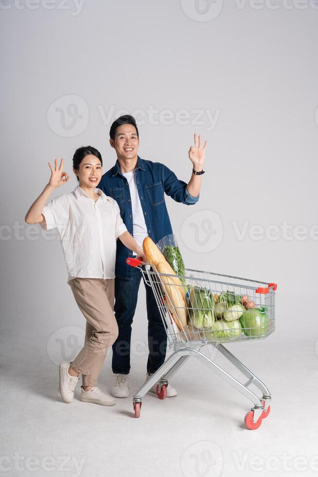 Image of Asian couple pushing supermarket cart while shopping, isolated on white background photo