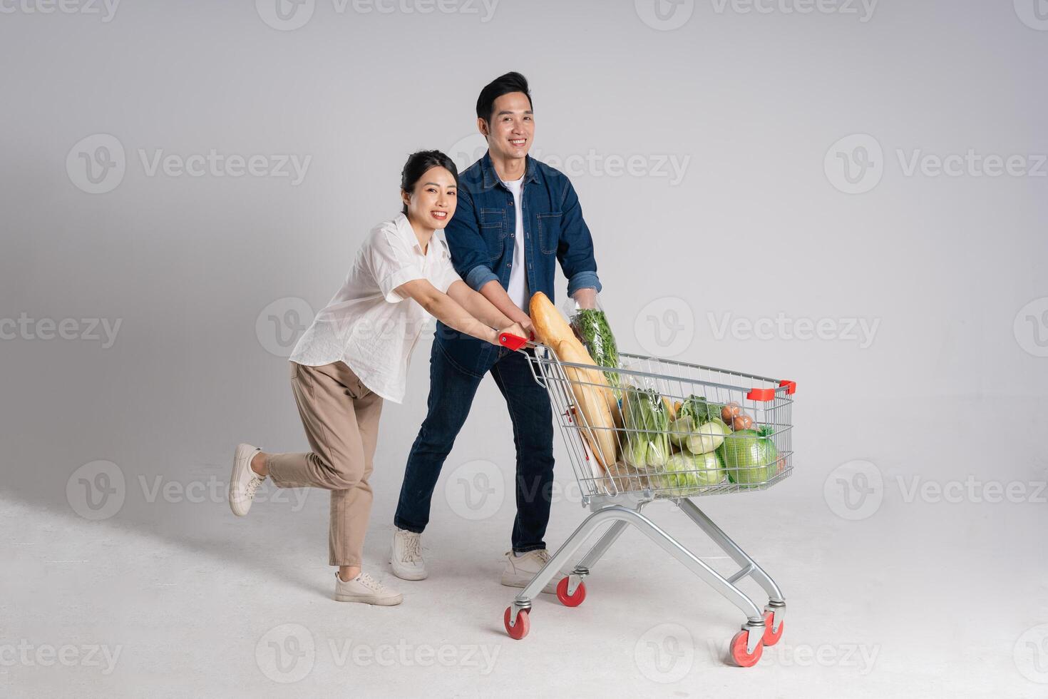 Image of Asian couple pushing supermarket cart while shopping, isolated on white background photo