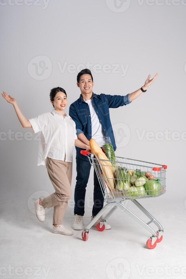 Image of Asian couple pushing supermarket cart while shopping, isolated on white background photo