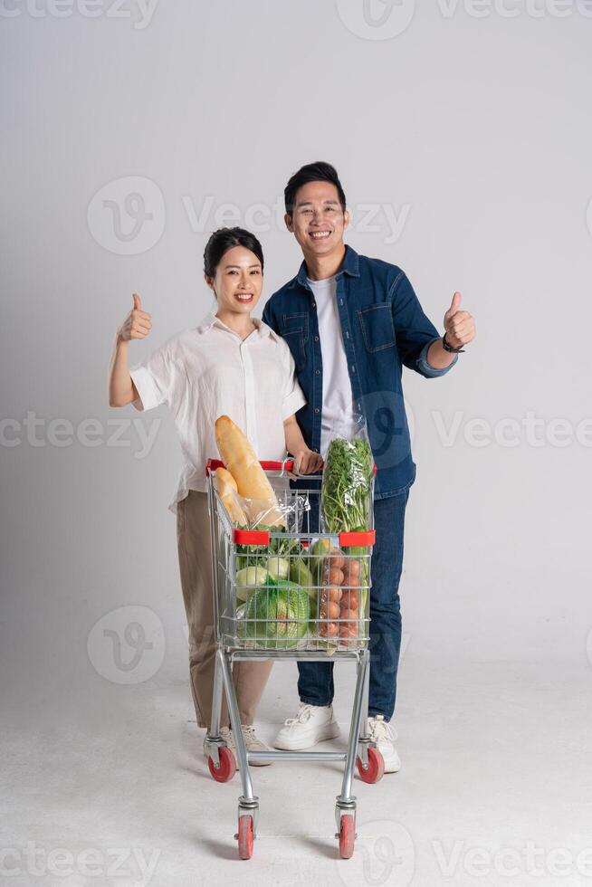 Image of Asian couple pushing supermarket cart while shopping, isolated on white background photo