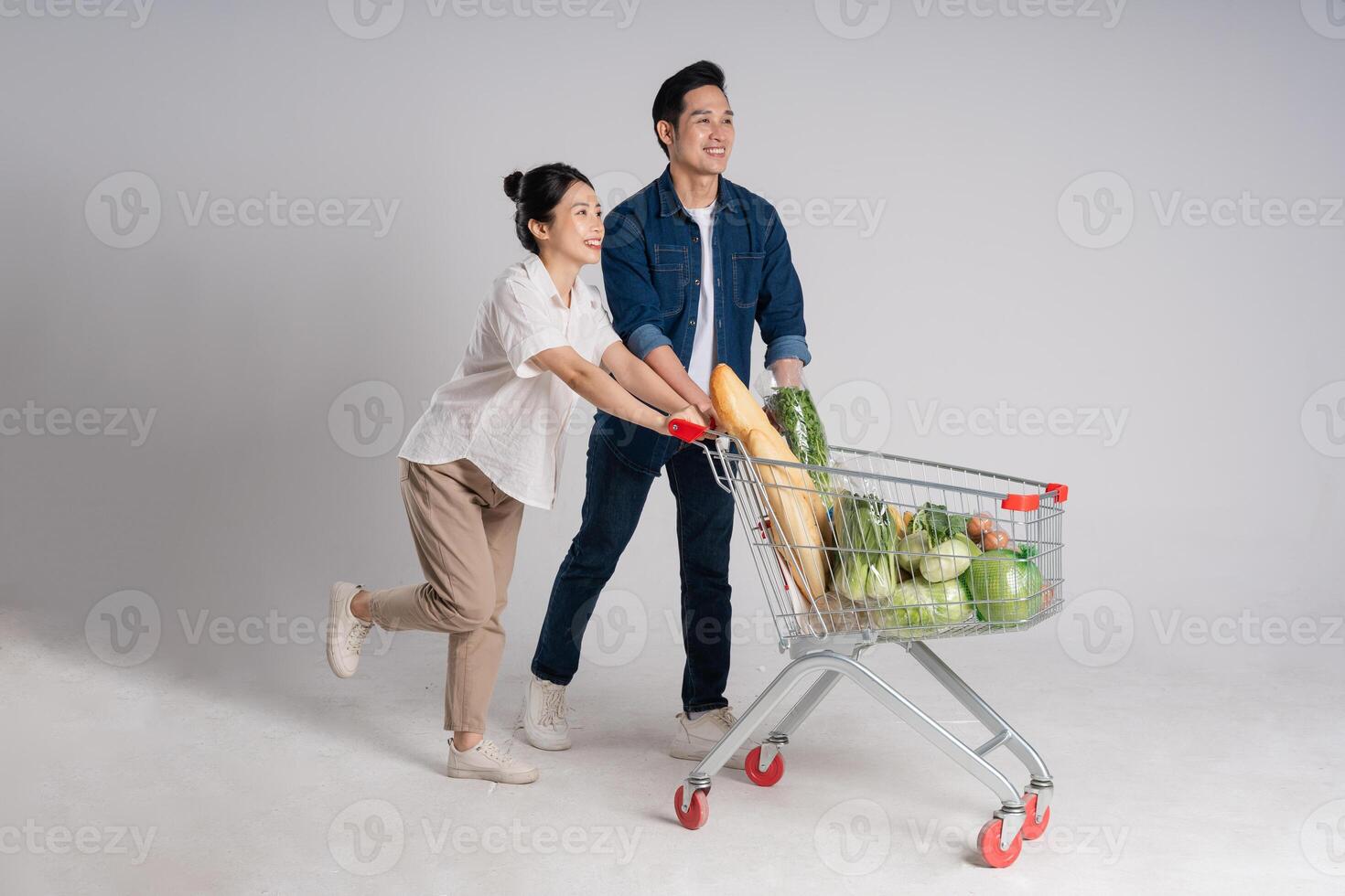 Image of Asian couple pushing supermarket cart while shopping, isolated on white background photo