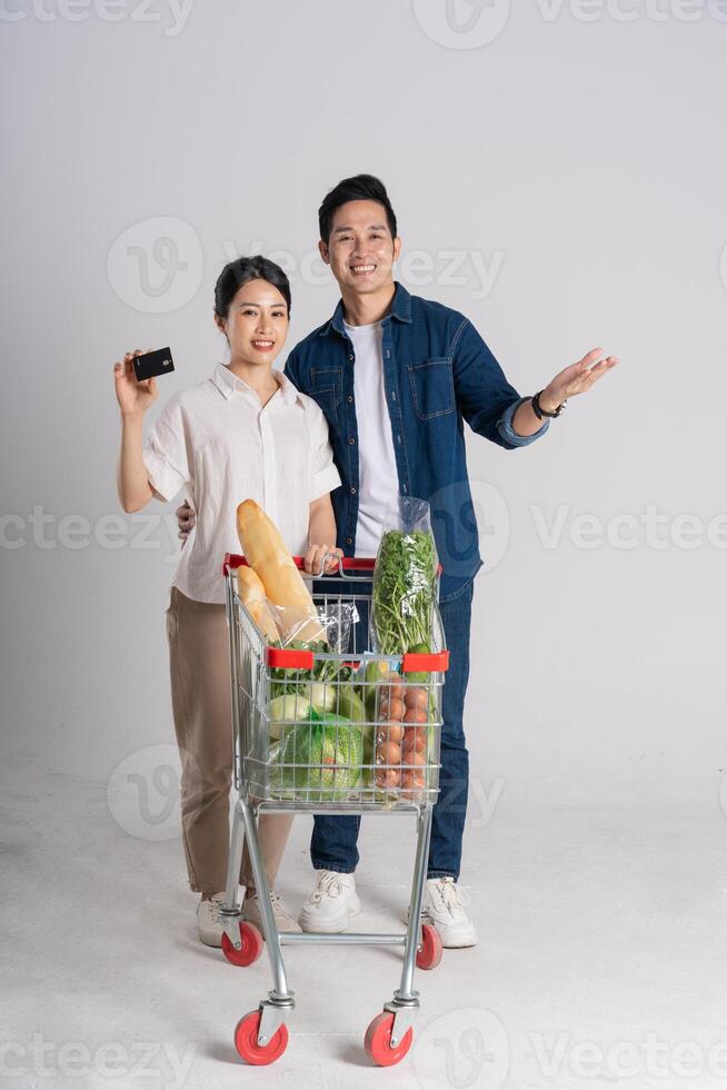 Image of Asian couple pushing supermarket cart while shopping, isolated on white background photo