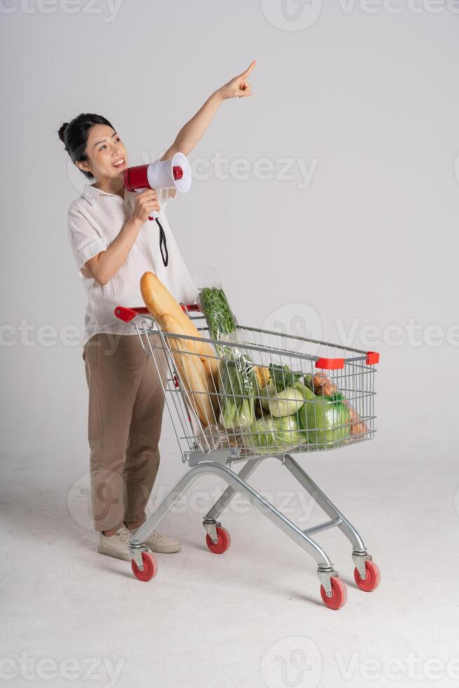 sonriente mujer felizmente emprendedor un supermercado carro, aislado en blanco antecedentes foto