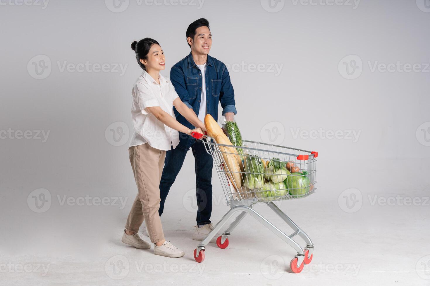 Image of Asian couple pushing supermarket cart while shopping, isolated on white background photo