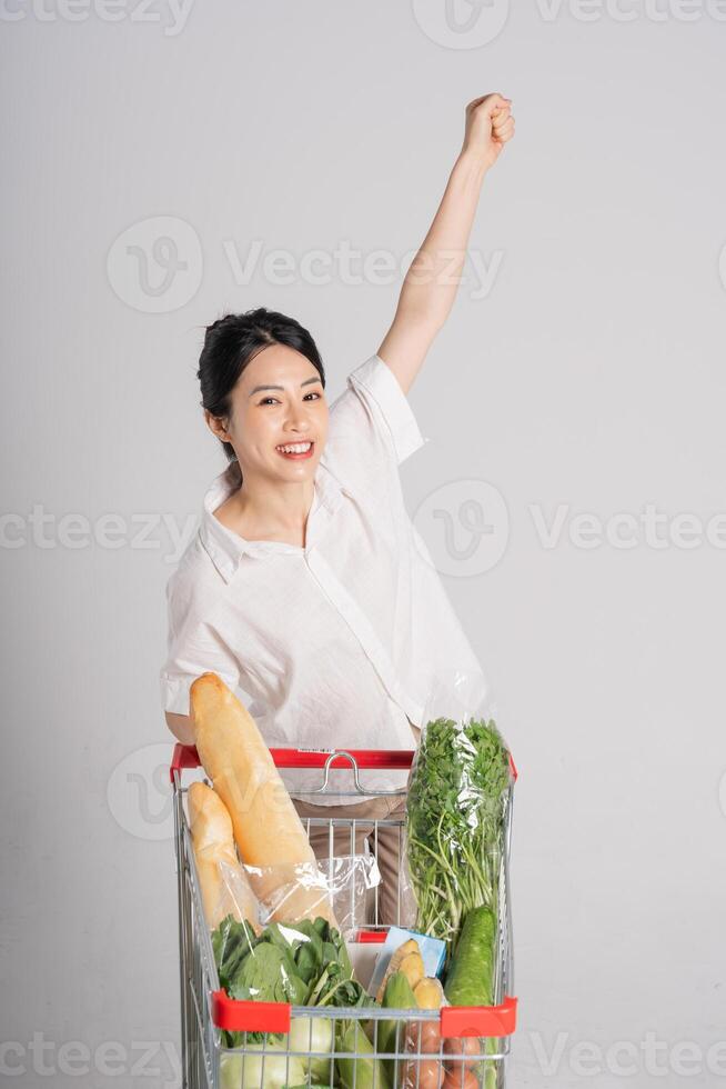 sonriente mujer felizmente emprendedor un supermercado carro, aislado en blanco antecedentes foto