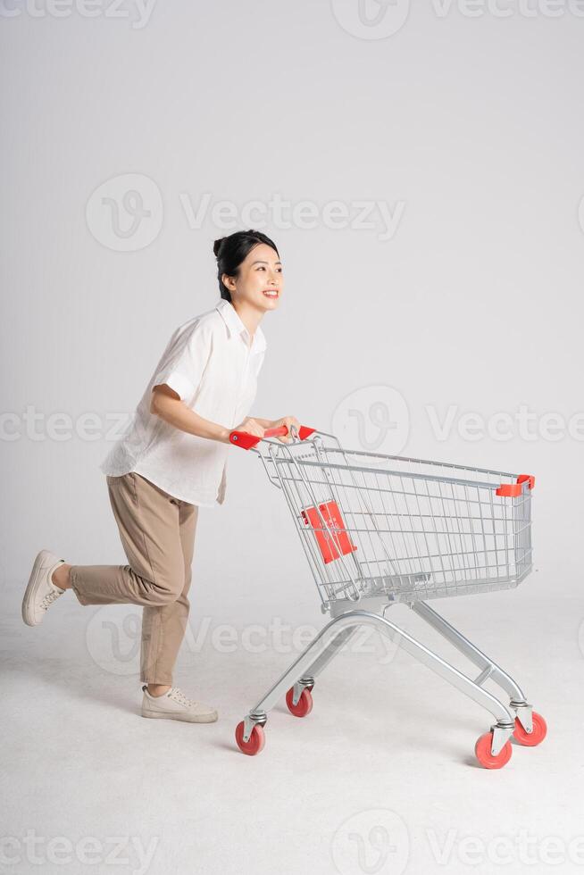 Smiling woman happily pushing a supermarket cart, isolated on white background photo