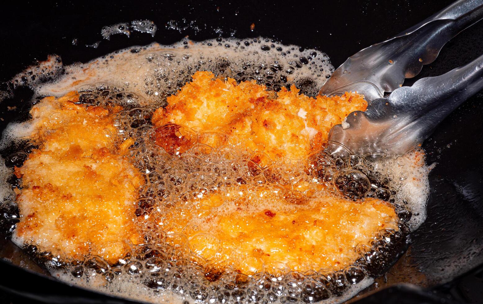 empanizado frito pollo. comidas frito en hirviendo petróleo en un chino wok Cocinando por fritura en caliente aceite. burbujas Aparecer desde fritura foto