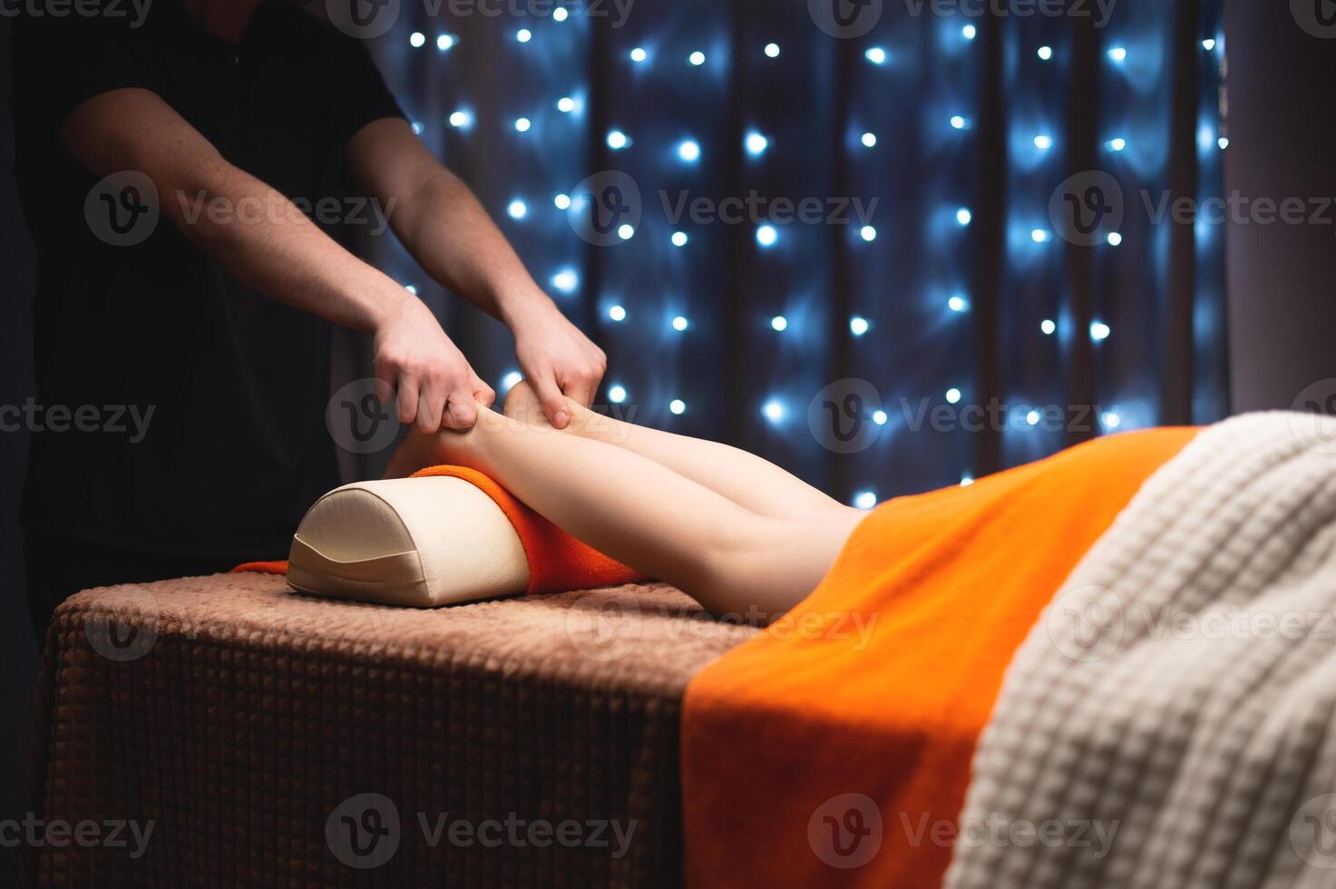 Close-up in shallow depth of field of a male masseur's hands massaging the Achilles tendon of a female leg. Professional massage in a professional room photo