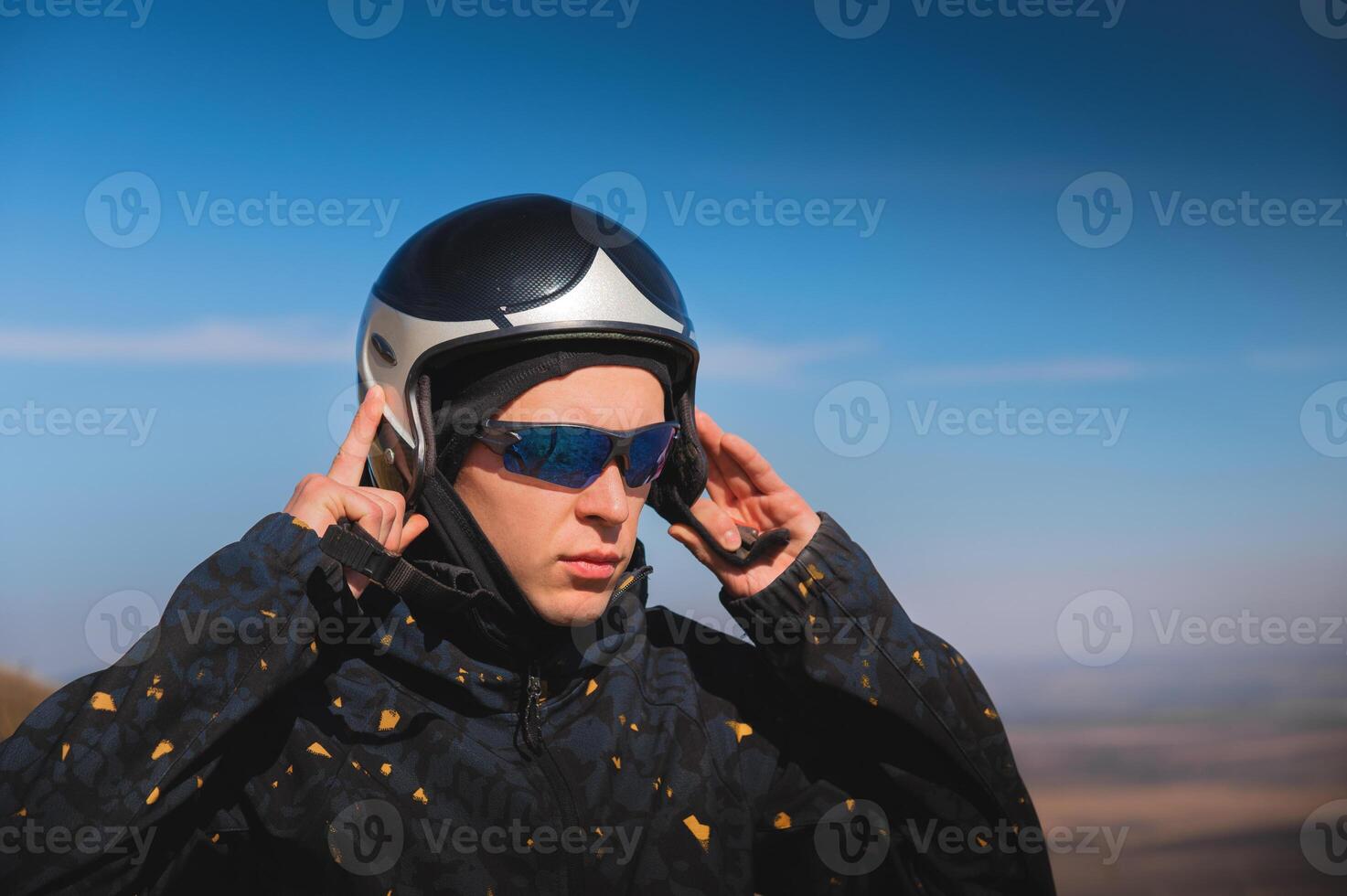 A young male paraglider in sunglasses fastens his helmet on a sunny day. Preparing for paragliding photo