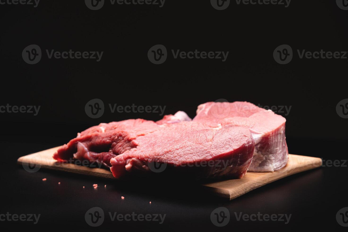 piece of raw beef in a slice on a wooden cutting board, on a black background. Procuring food photo