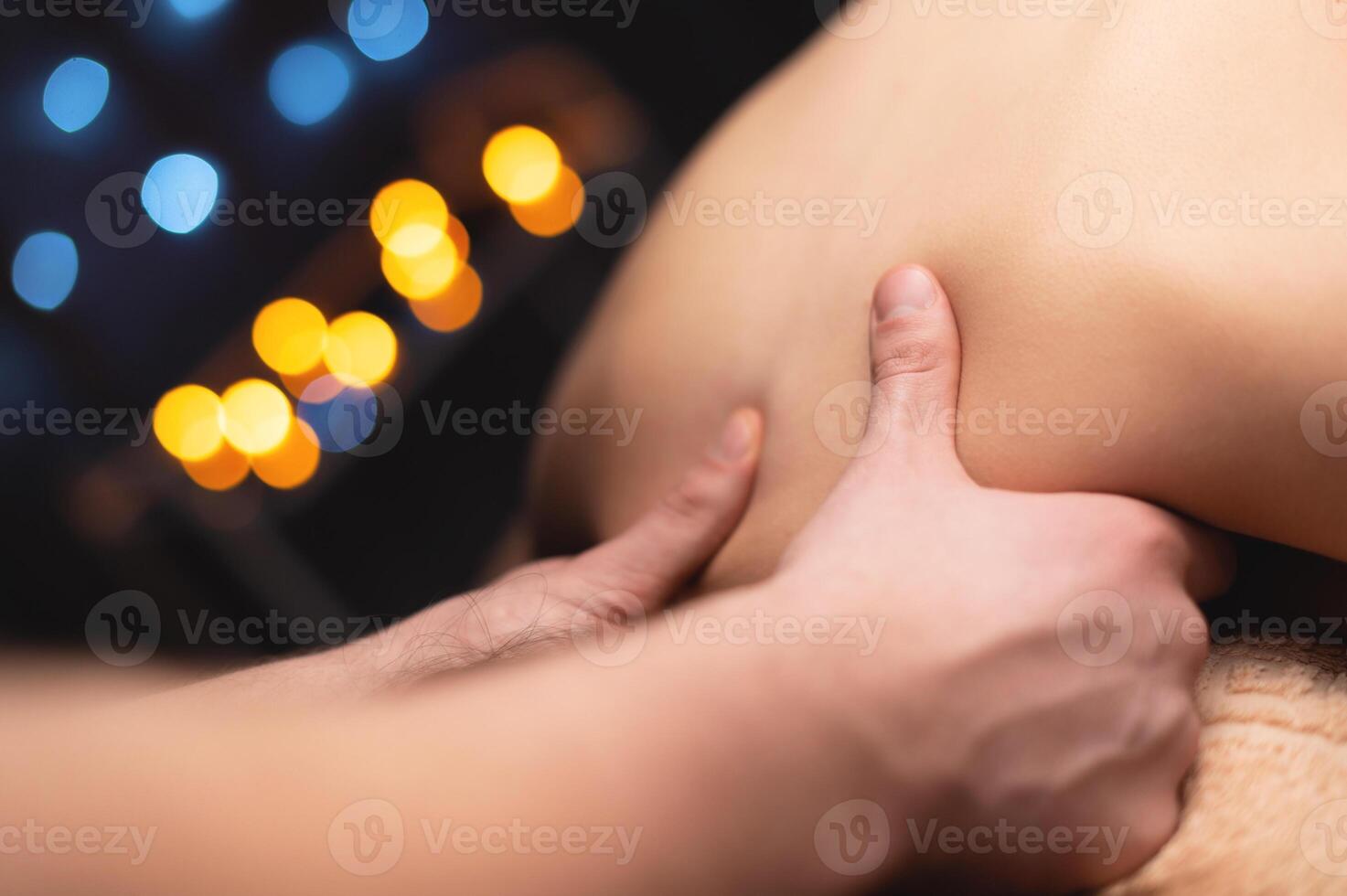 Close-up of a woman's neck and trapezium being massaged by a male masseur in shallow depth of field photo