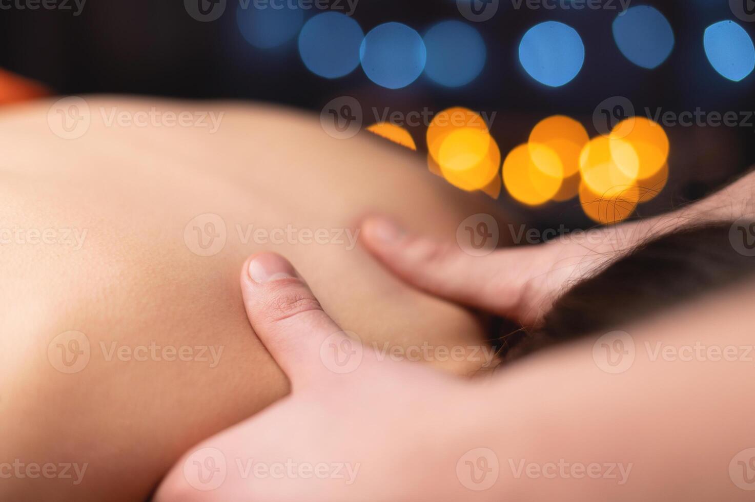 Close-up of a woman's neck and trapezium being massaged by a male masseur in shallow depth of field photo