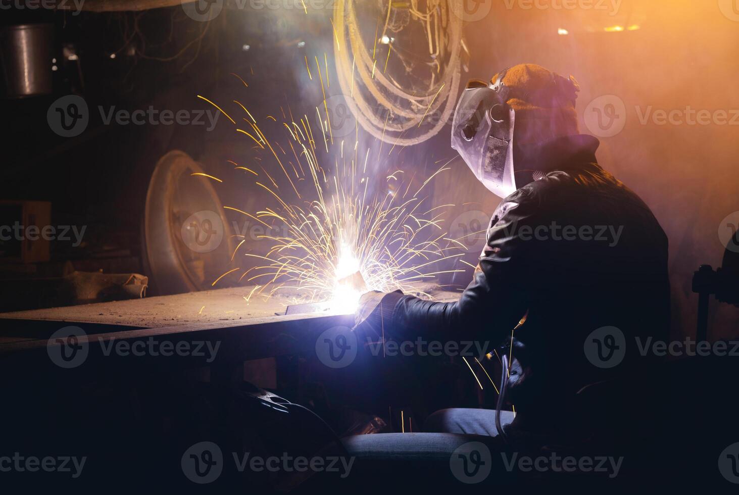 Young mechanic with a welding machine in an old dirty garage at night. Man in protection doing welding work, hobby photo
