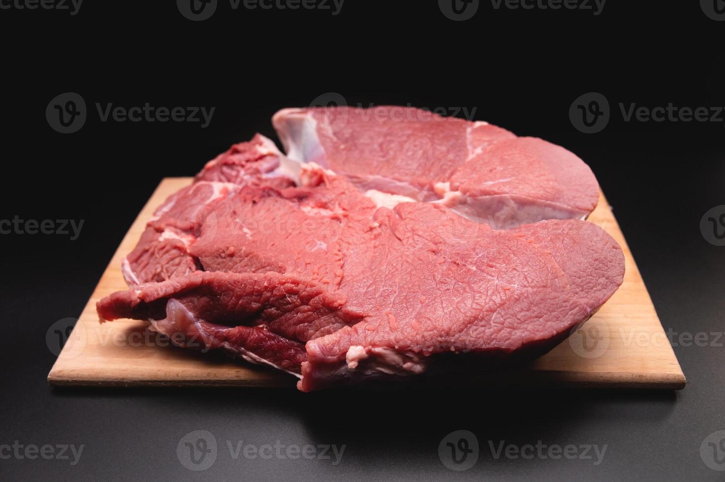 piece of raw beef in a slice on a wooden cutting board, on a black background. Procuring food photo