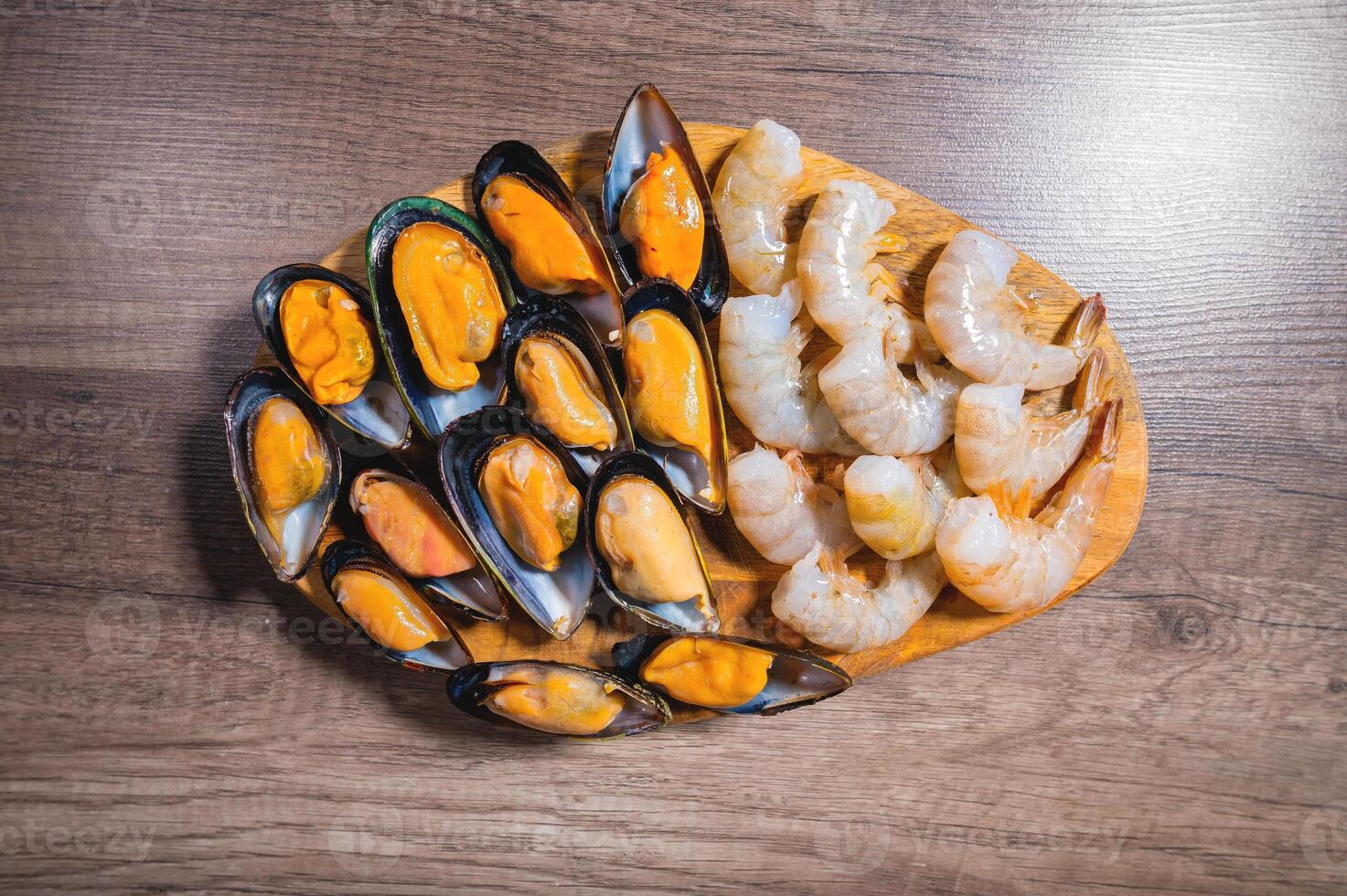 Flat kitchen table raw mussels and shrimp lie on a wooden plate. Sea food. Mediterranean diet photo