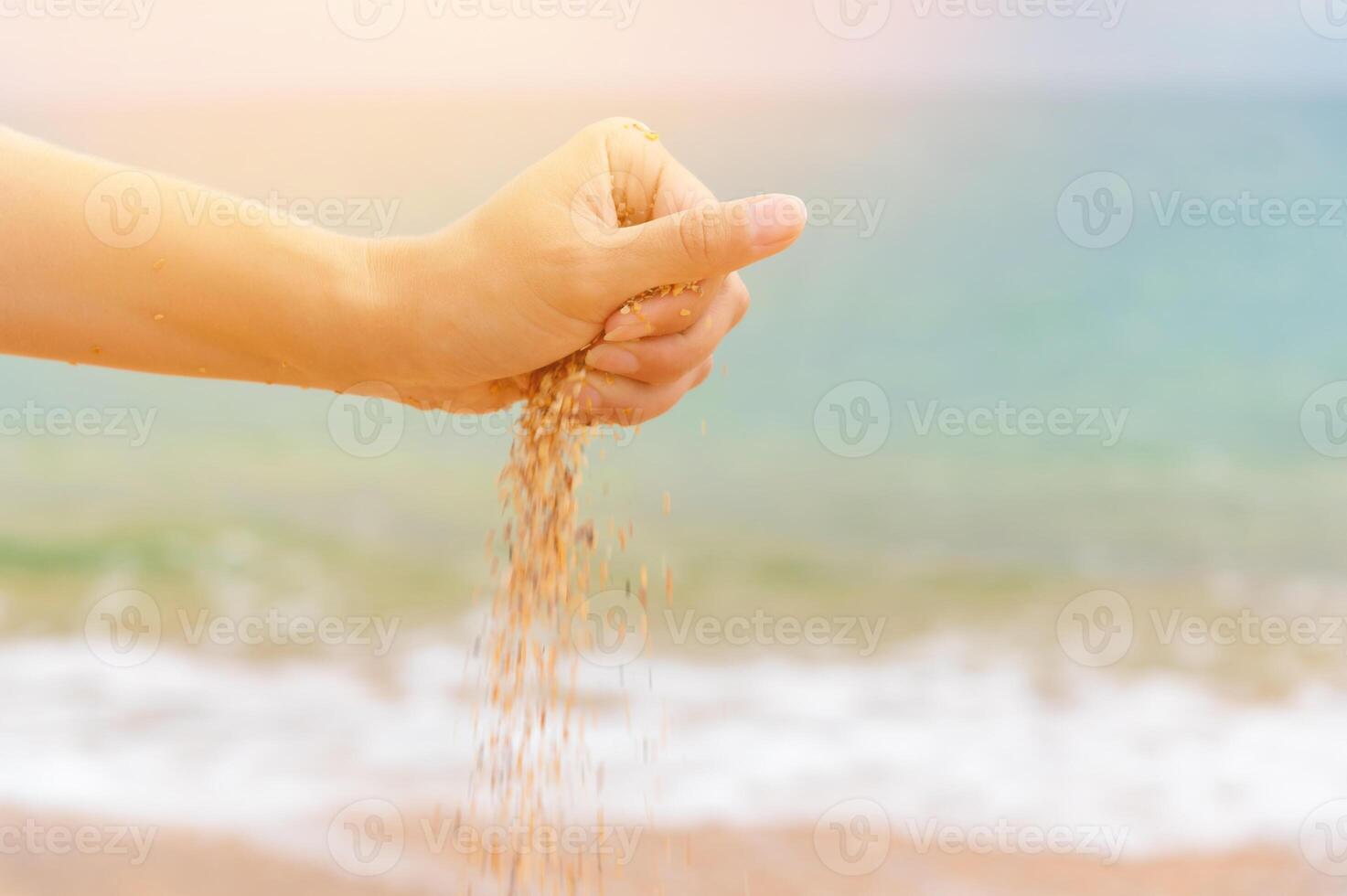 Sand falls from woman hands on sea summer background photo