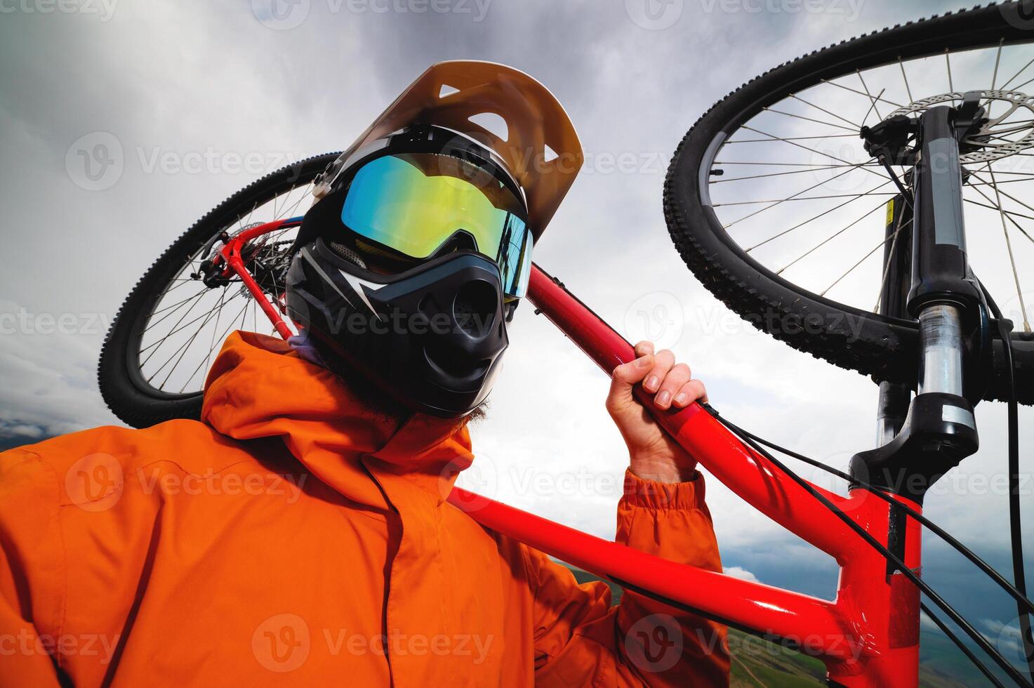 amplio ángulo vertical marco parte superior ángulo. retrato de un barbado montaña motorista con su bicicleta en contra un antecedentes de montañas y nubes en el verano rodeado por verde césped foto