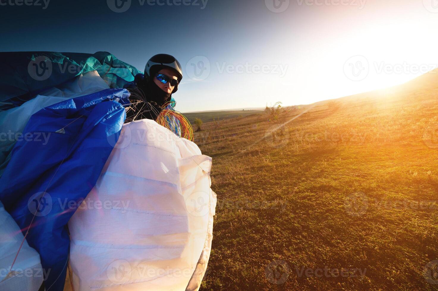 A young male paraglider at sunset in the mountains collects his paraglider to take it to the starting point. Paragliding sport photo