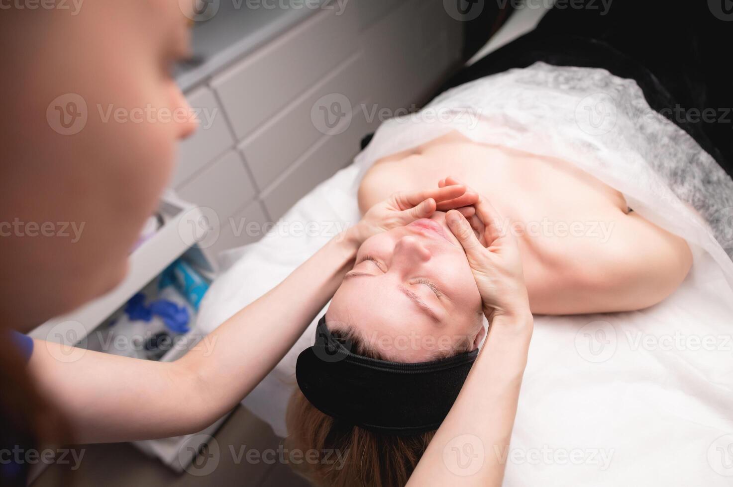 de cerca Disparo de un mujer cabeza haciendo un facial masaje en un tratamiento mesa. terapeuta aplicando presión con pulgares en frente foto