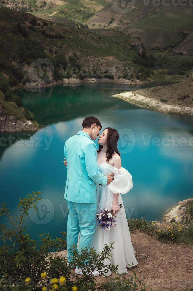 hermosa Boda Pareja abrazos tiernamente en contra el fondo de un montaña río y lago, el de la novia largo blanco vestir foto