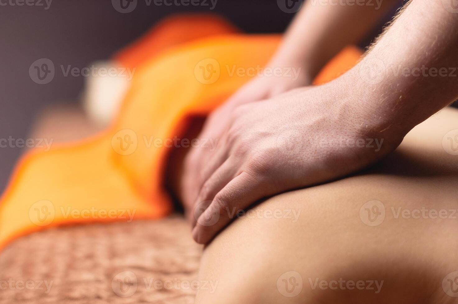 Close-up shot of an unrecognizable male masseur making massage movements on the back of a young woman, preventing spinal pain, lying on a massage table in a spa salon. Body care concept photo