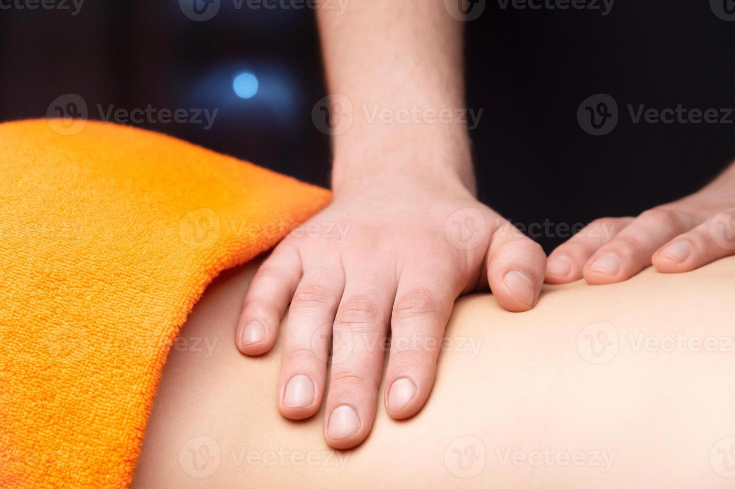 Close-up Side view in shallow depth of field. Massage of the lower back by a male masseur. Volumetric light. Live photography photo