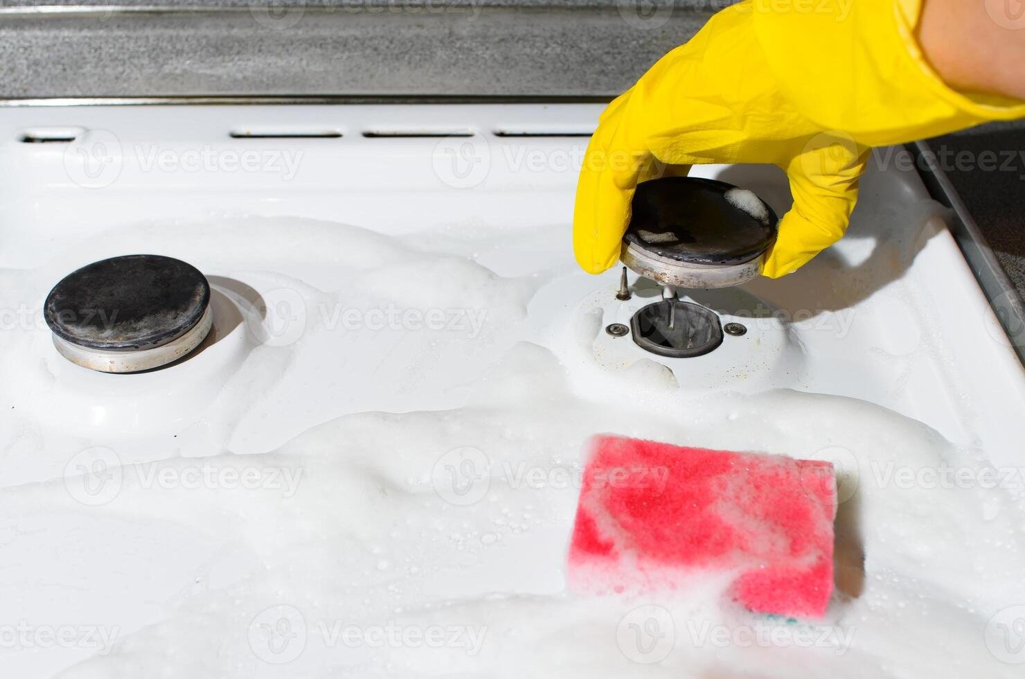 Woman cleans the gas stove close-up. Woman's hand in glove washing burner photo