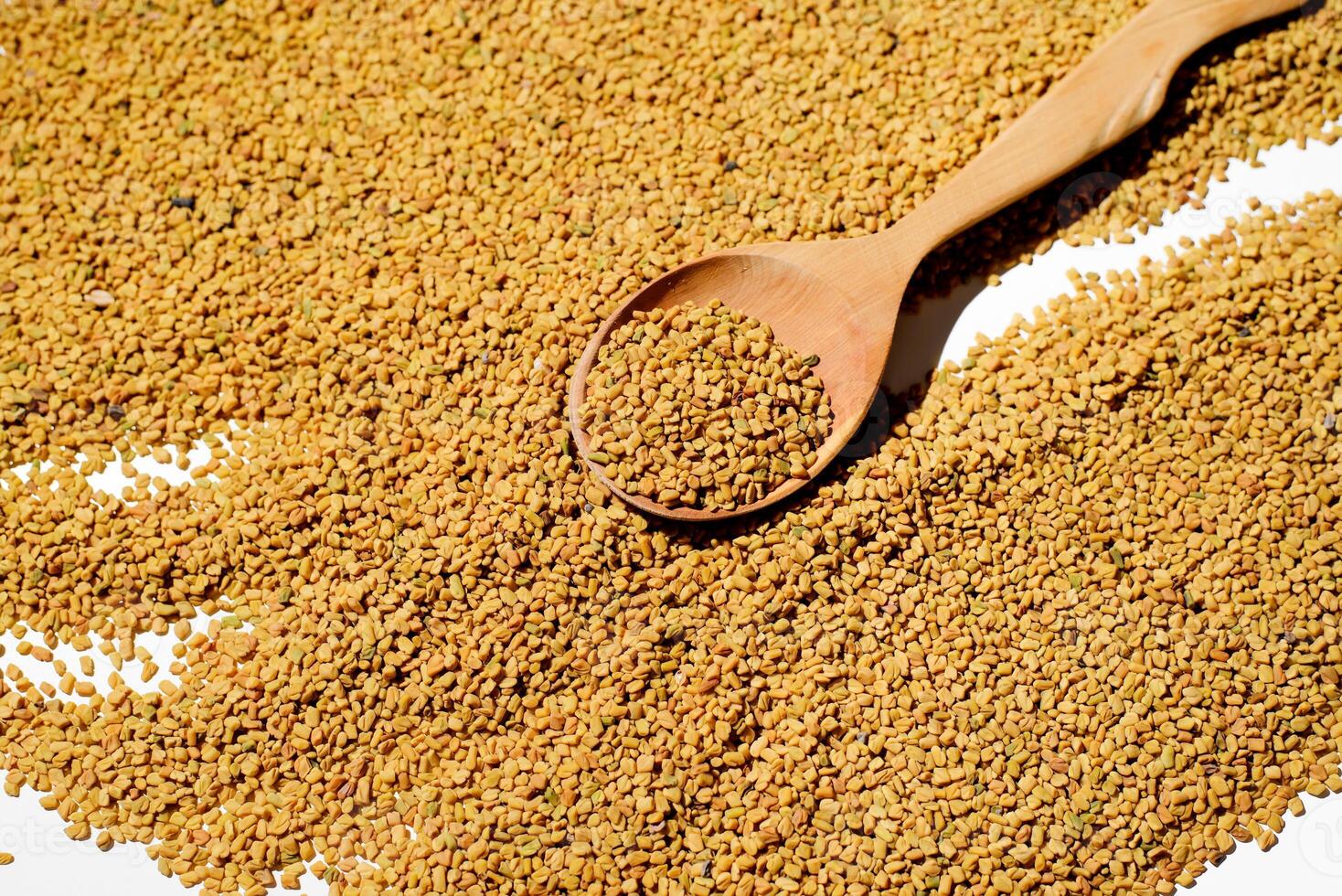 Fenugreek spoon on a background of scattered grains yellow tea, top view photo