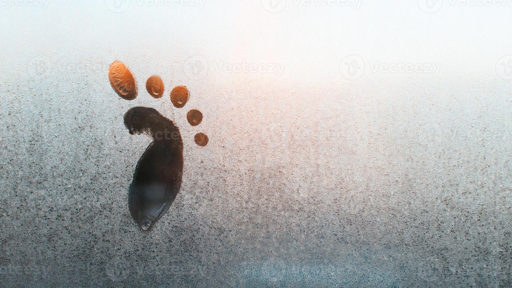 Drawing of a child's foot on a frozen window, copy space. Frosty pattern on glass. Funny creative concept. Textured ice surface. photo