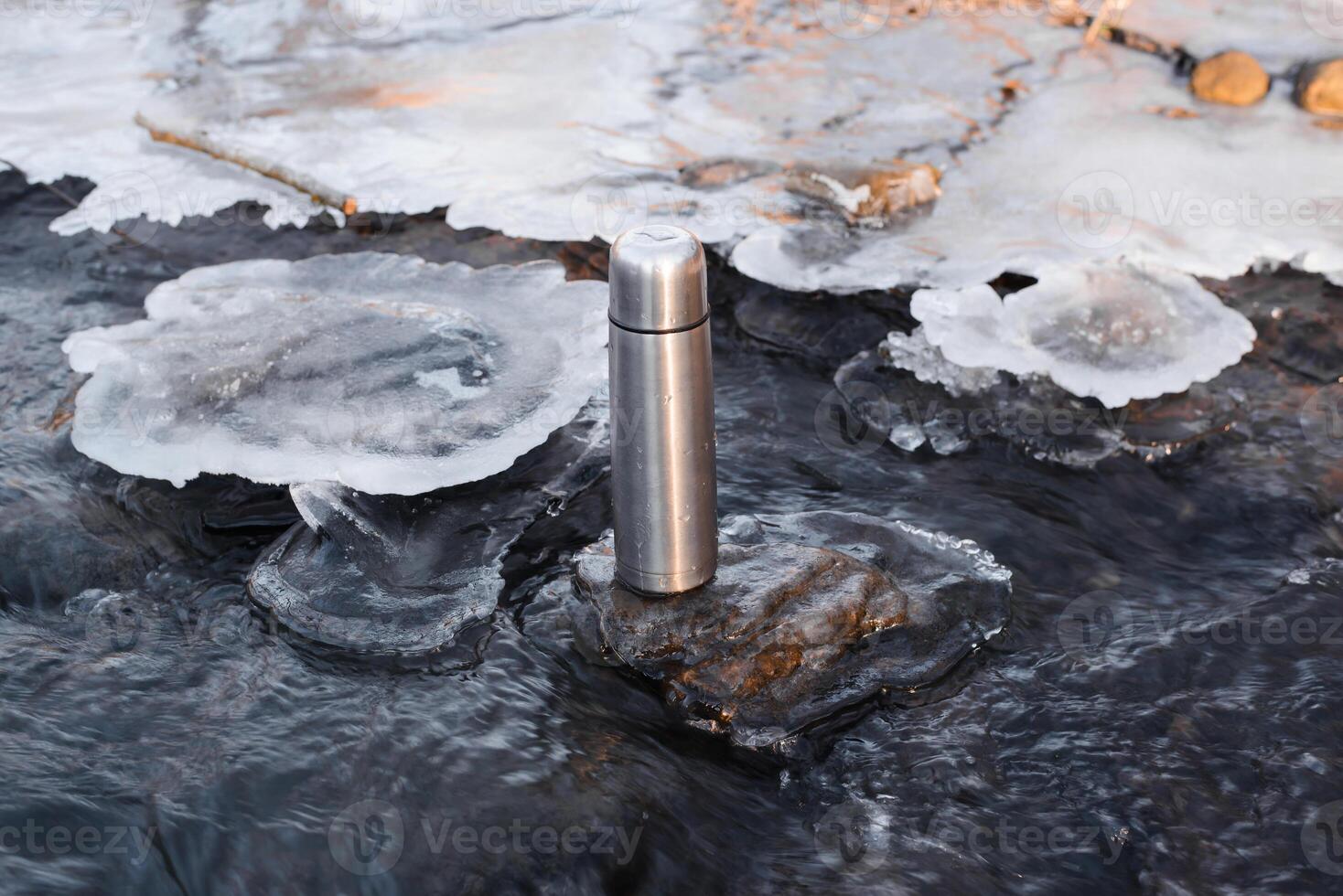 Thermos standing in a winter stream. Vacuum steel flask for hiking. Travel concept, warming drink in winter. photo