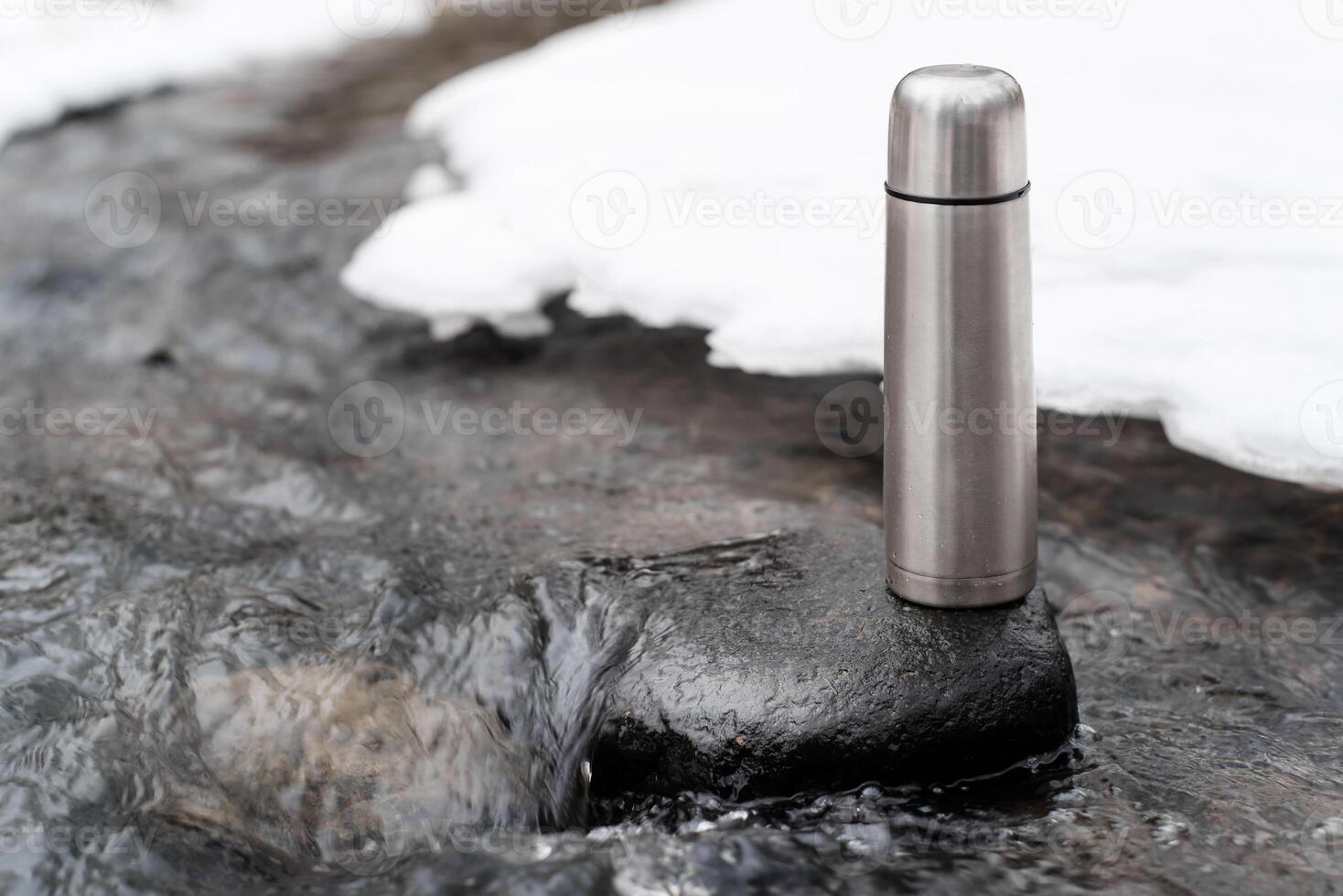Thermos standing in the stream. Camping vacuum thermos outside in winter, copy space. Adventure concept, winter hike, travel. photo