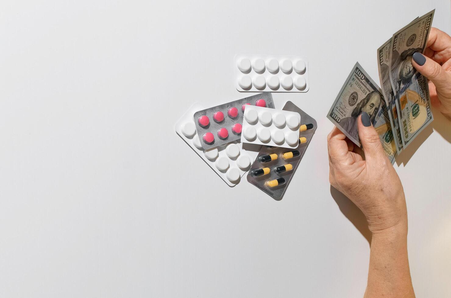 Elderly woman's hands holding money. Tablets on white table top view, copy space. Concept of treatment cost, medicine price, health insurance budget photo