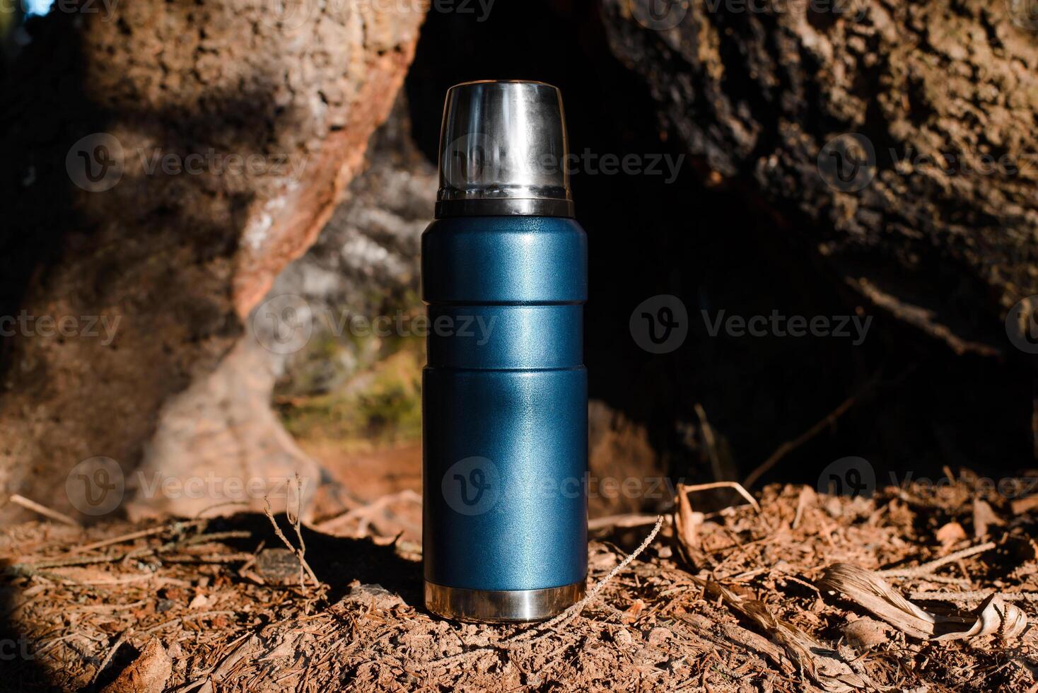 Thermos standing in a sunny forest. Vacuum travel flask close up. Camping concept, equipment for travel, adventure. photo