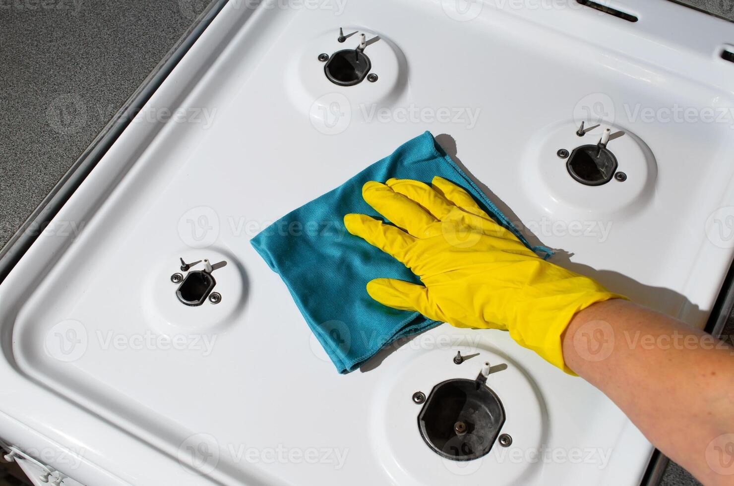 Woman washing gas stove. Woman's hand in glove wipes the gas panel with rag, top view. Cleaning of kitchen apartments photo