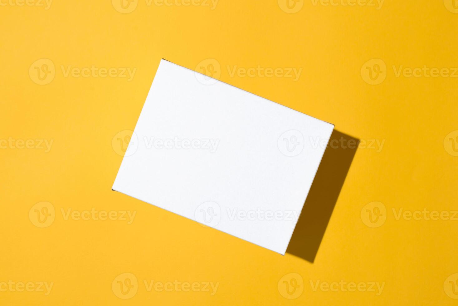 White box mockup on yellow background, flat lay. Blank surface of small cardboard box top view, copy space. photo